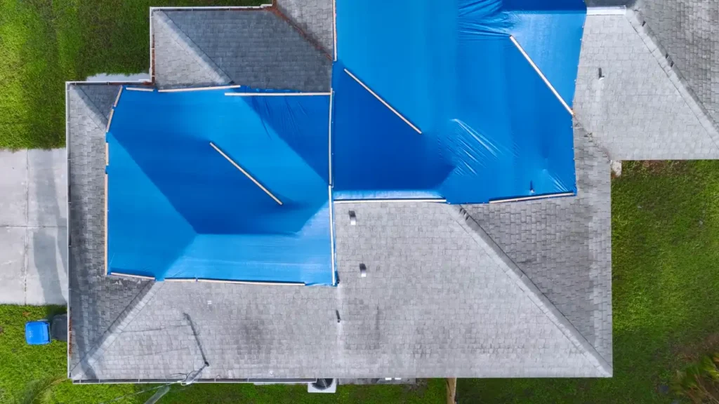 Aerial view of blue tarps fastened over the damaged slopes of a roof after a storm