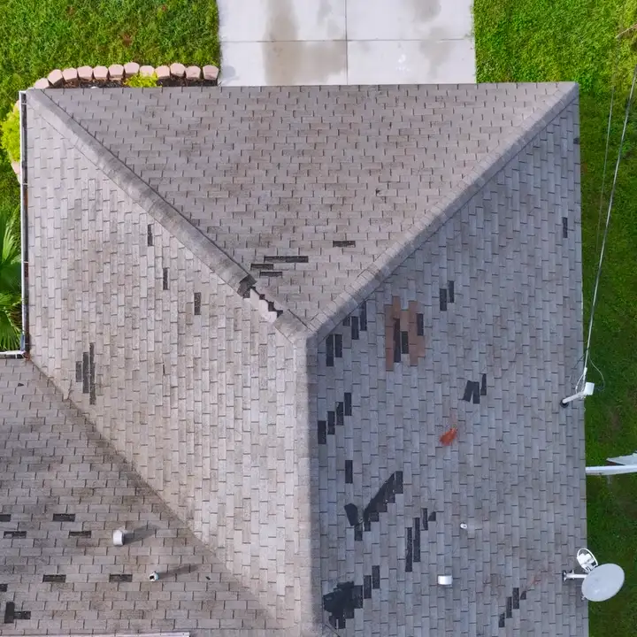 Wind-damaged shingle roof with missing shingles before repair