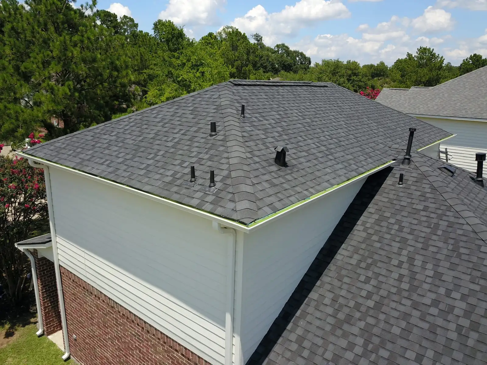 Hip and ridge lines of a new dark gray shingle roof with roof vents on a two-story home in Conroe, TX, seen from above